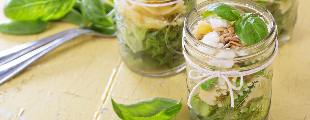 Pasta salad in jars with farfalle, salad greens, peas and feta